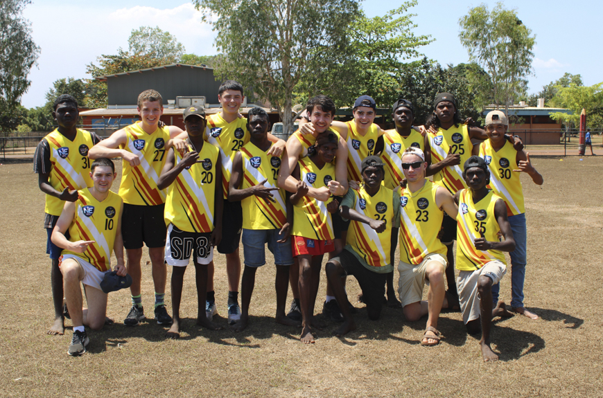 A group of students from Tiwi College and Scotch College in AFL jumpers smiling and looking towards the camera