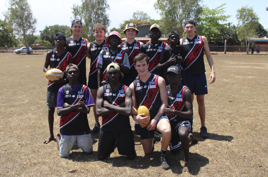 A group of students from Tiwi College and Scotch College in AFL jumpers smiling and looking towards the camera